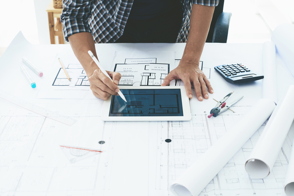 Hands,Of,Architect,Using,Tablet,Computer,When,Working,On,Blueprint